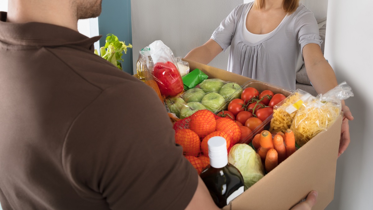 Delivery man hands box of groceries to woman at her front door